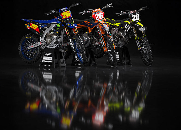 Four motocross bikes with visible branding on a reflective black surface